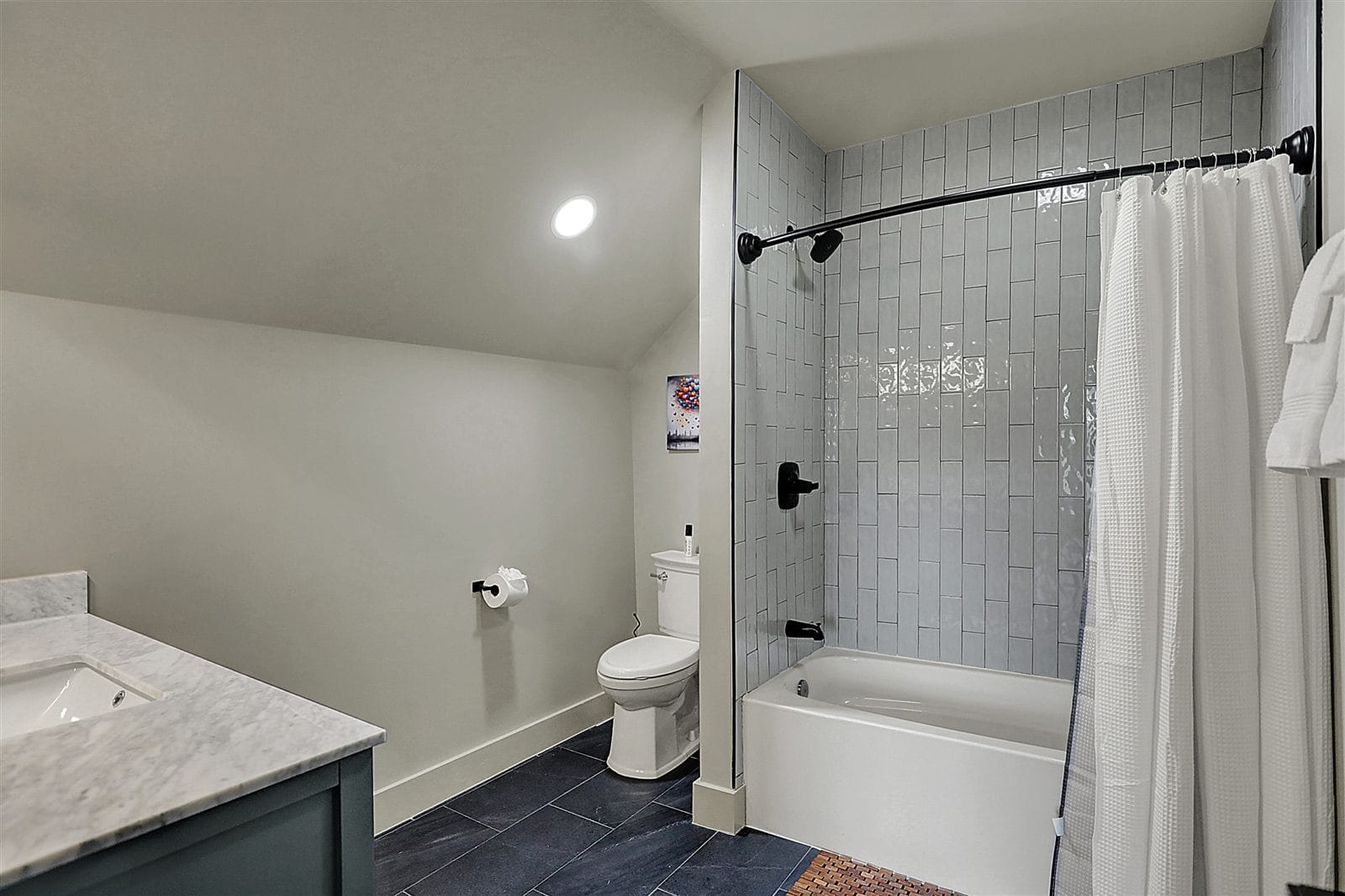 Upstairs hall bath with tub-shower combo, vertical subway tile, and dark slate flooring