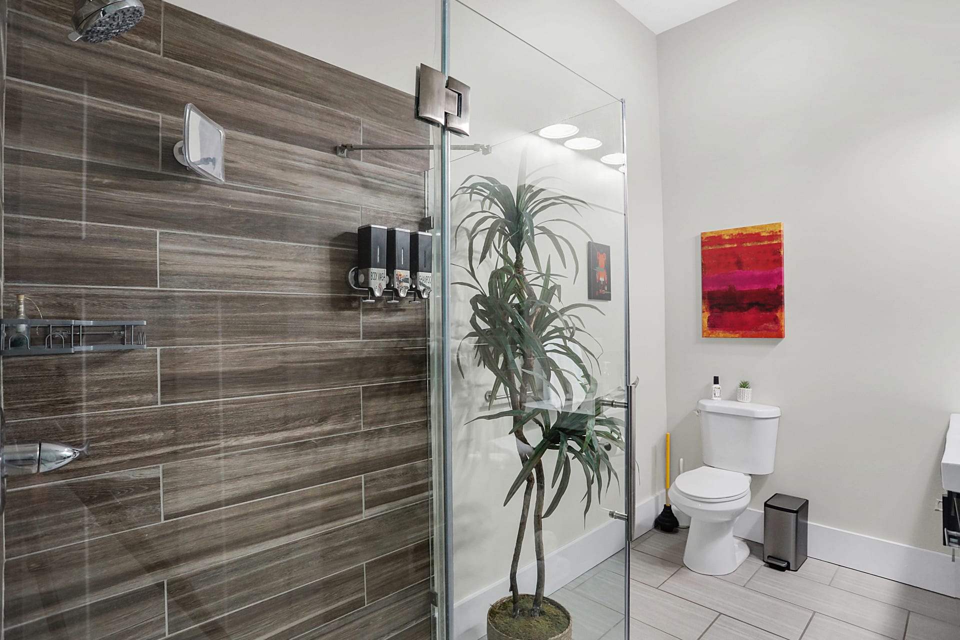 Primary ensuite bathroom with frameless glass shower, wood-look tile, and freestanding toilet at The Sanders