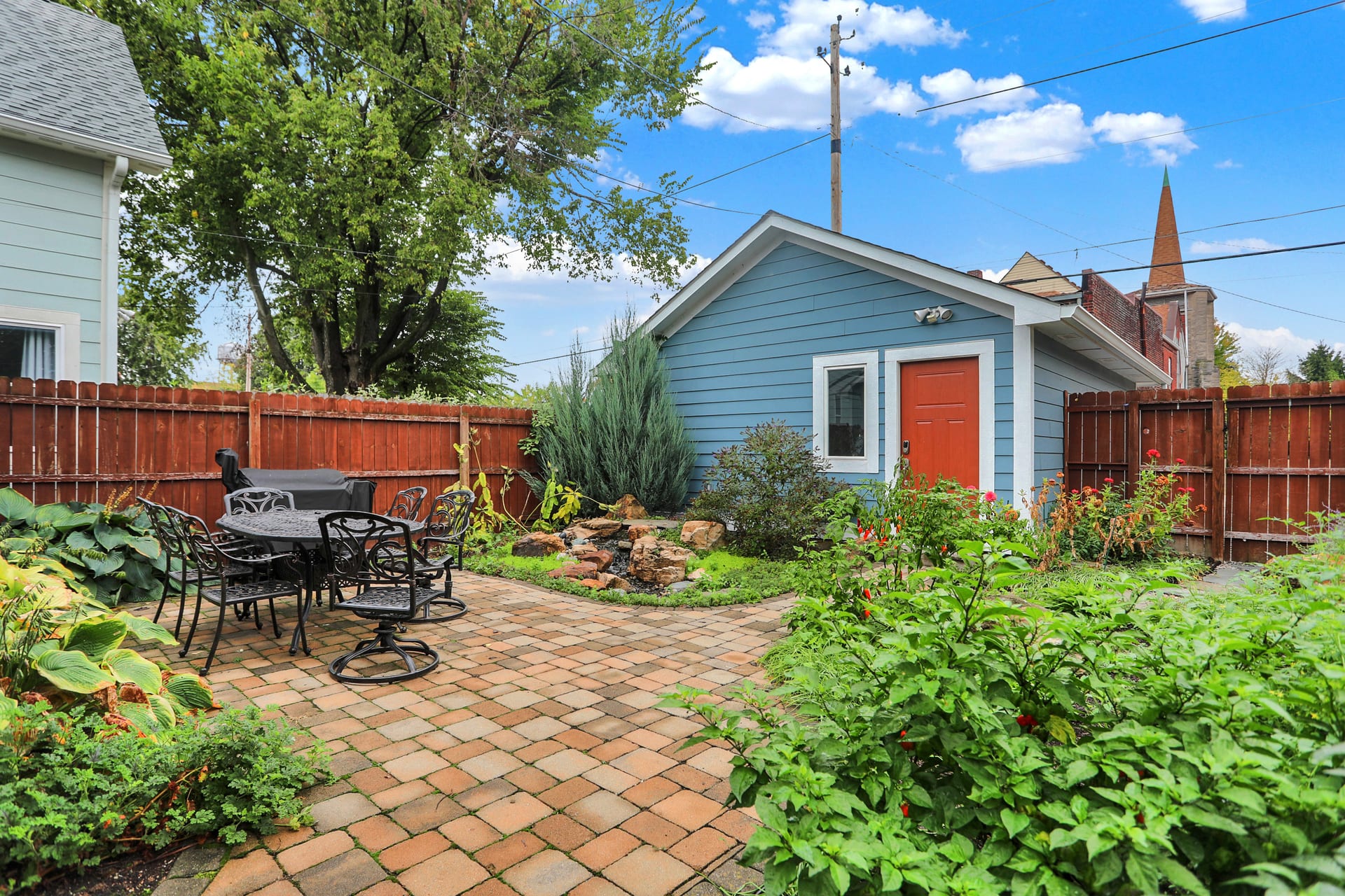 Fully fenced backyard with paver patio, cast-aluminum dining table, and the detached garage beyond