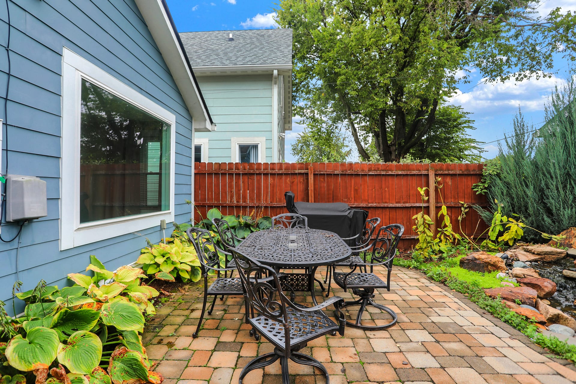 Patio dining for six beside the pond and Traeger grill, with mature hostas along the house