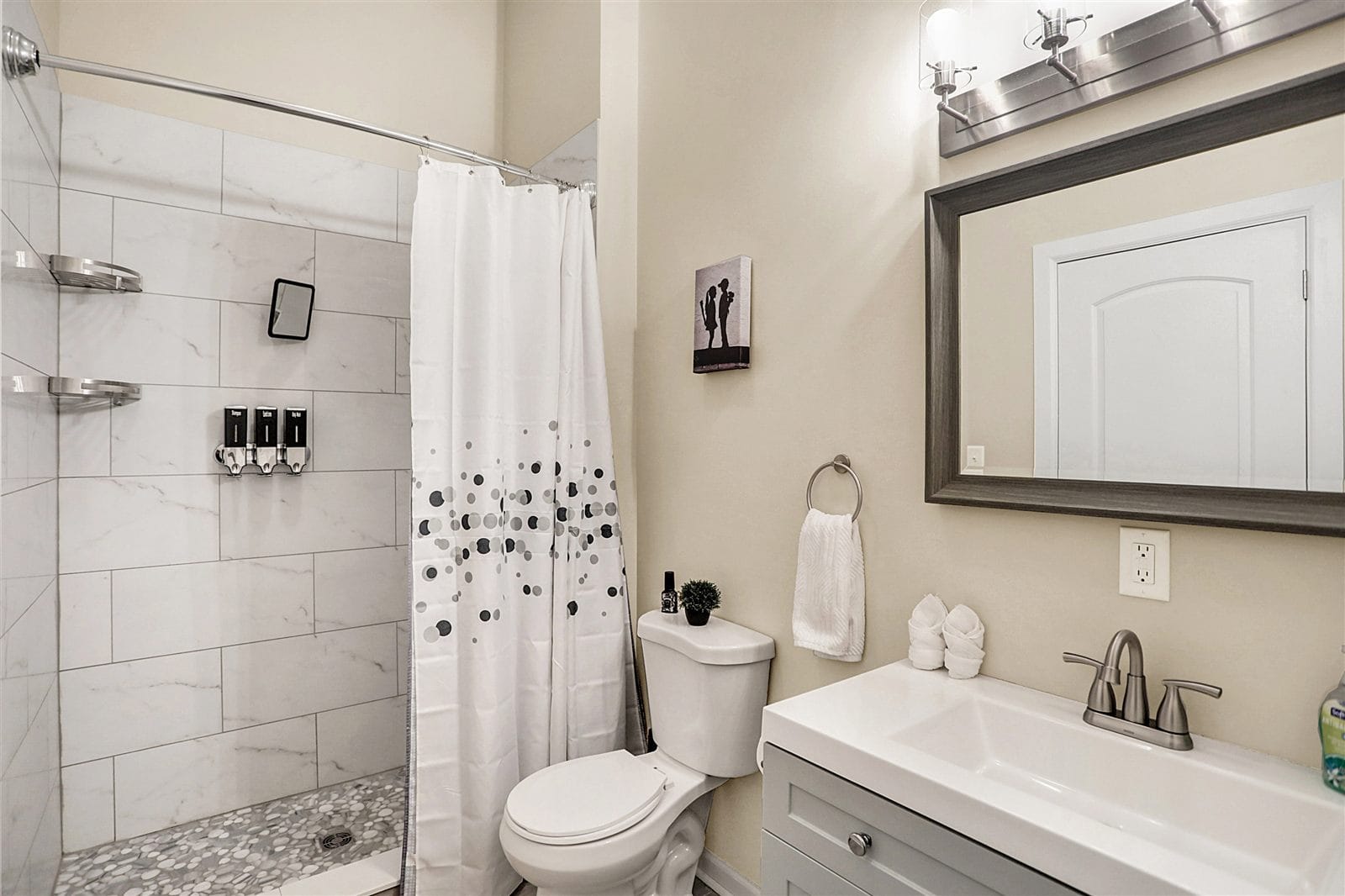 Hall bathroom with marble-tile walk-in shower, gray vanity, and Banksy-style art